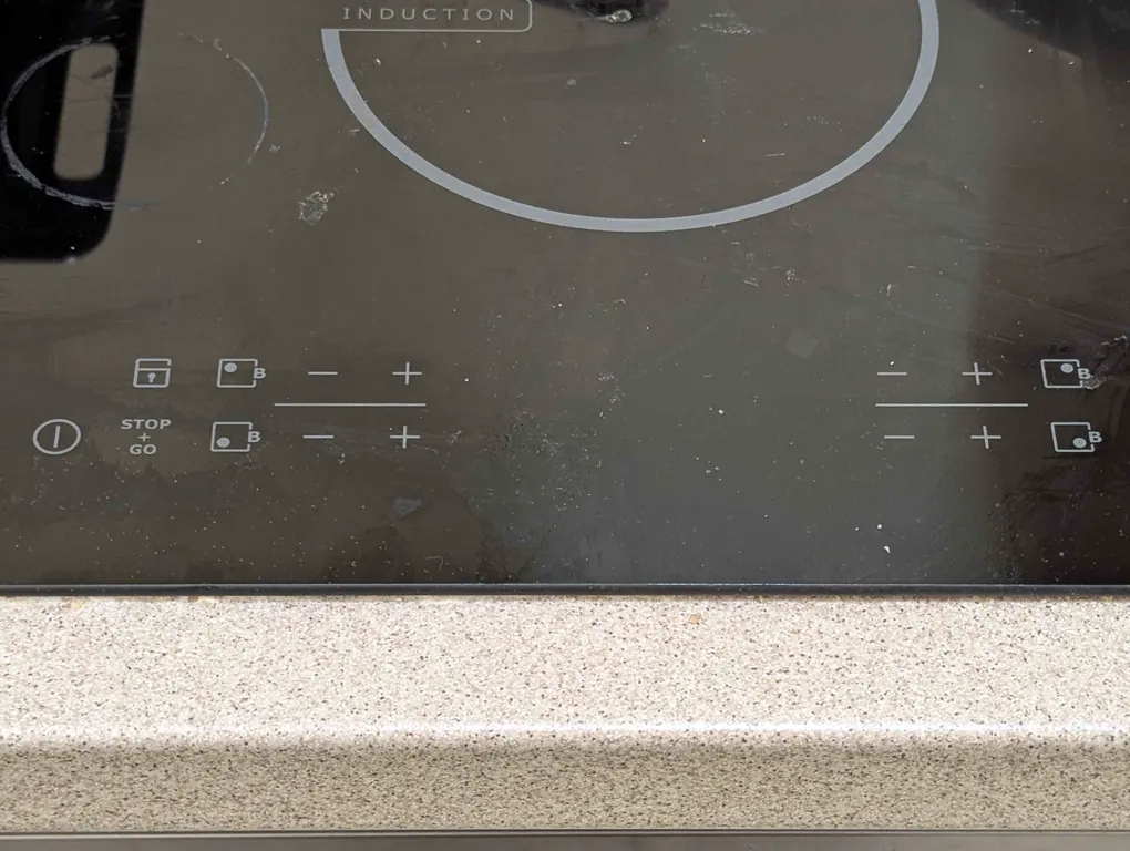 close-up of an induction stove’s touch panel. there’s a power button, buttons for controlling each of the four burners’ power levels, a lock button, and a “stop + go” button.